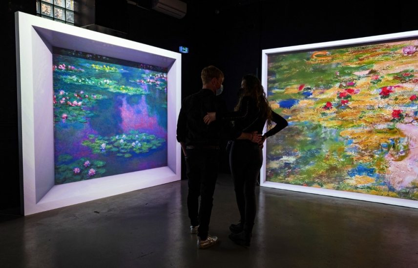 A couple looks at projections featuring works by French painter Claude Monet (1840-1926), part of the "Monet's Garden" exhibition in Berlin on January 31, 2022. - The exhibition, which opened on January 12, 2022, mixes multimedia technology, installations and projections, combined with music, in a a bid to "bring the paintings to life in ways never before seen." (Photo by John MACDOUGALL / AFP) / RESTRICTED TO EDITORIAL USE - MANDATORY MENTION OF THE ARTIST UPON PUBLICATION - TO ILLUSTRATE THE EVENT AS SPECIFIED IN THE CAPTION