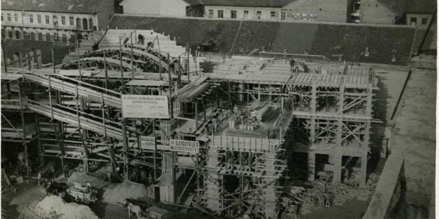 A szomszédos házból felvéve, az Asbóth utcai szárny váza két emelet magasságig kész, a tervezett Madách sugárutat megnyitó kapuzat boltívét zsaluzzák. Rálátás az építkezés mögötti házakra