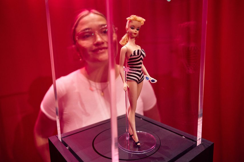 A gallery assistant poses with the original first edition Barbie doll from 1959 during the "Barbie: The Exhibition" photocall at The Design Museum in London on July 1, 2024. (Photo by BENJAMIN CREMEL / AFP) / RESTRICTED TO EDITORIAL USE - MANDATORY MENTION OF THE ARTIST UPON PUBLICATION - TO ILLUSTRATE THE EVENT AS SPECIFIED IN THE CAPTION