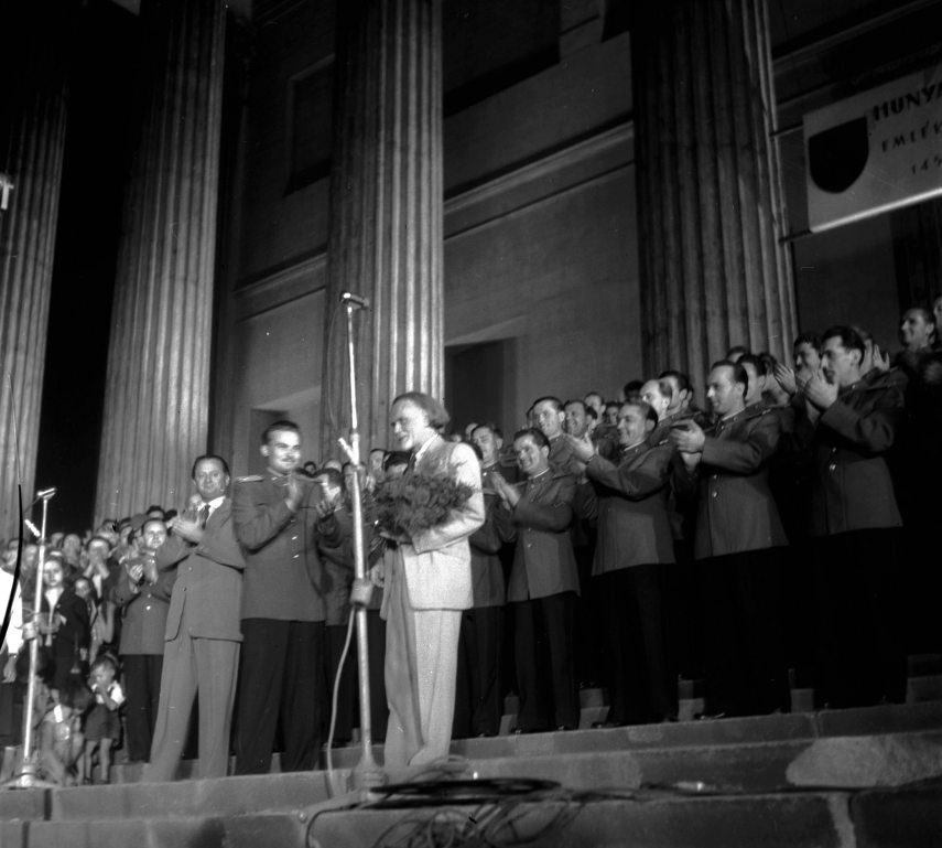 Budapest, 1956. szeptember 6. 
Kodály Zoltán zeneszerző és zenetudós, a Magyar Tudományos Akadémia tiszteletbeli tagja átveszi a Magyar Néphadsereg Művészegyüttesének nevében átadott virágcsokrot. Mellette a bal szélen Ortutay Gyula, művelődéspolitikus, néprajztudós és egyetemi tanár tapsol. Az énekegyüttes, mely szeptember 7-én indul kínai hangverseny-körútra, a Nemzeti Múzeum lépcsőjén bemutatta a nagyközönségnek Kodály új kórusművét, a "Nemzeti dal"-t. 
MTI Fotó: Zinner Erzsébet 