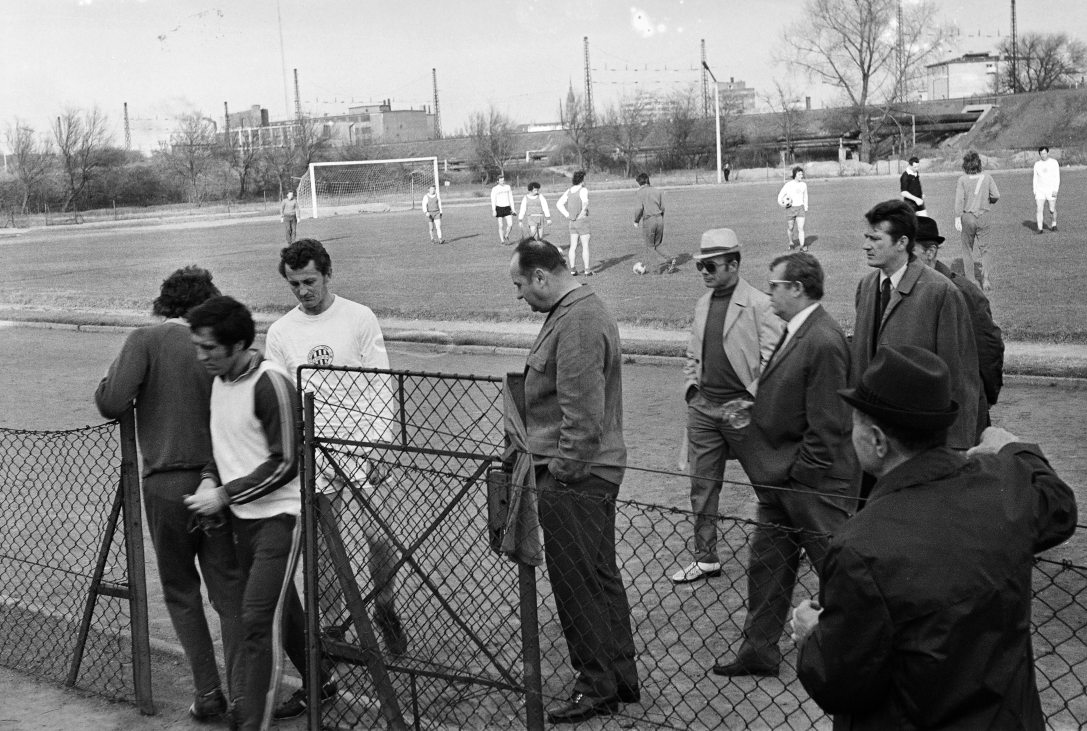Az FTC edzőpályája a Népligetben 1971-ben. A kerítés kapujánál Rákosi Gyula, a Ferencváros ikonikus középpályása, mögötte fehér szerelésben Albert Flórián, az egyetlen magyar aranylabdás labdarúgó. Fotó: Fortepan / Gyulai Gaál Krisztián