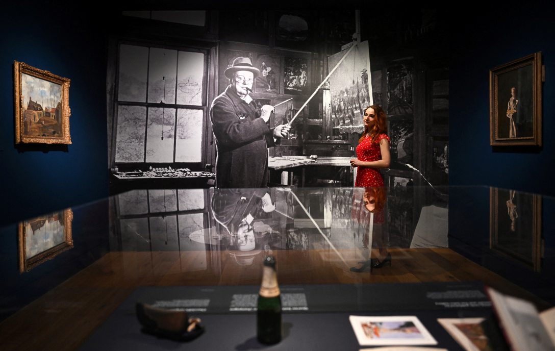 Galériaasszisztensek pózolnak Winston Churchill egykori festőállványa mellett a „Winston Churchill: A festő” című kiállításon a londoni Wallace Collection múzeumban 2026. május 20-án. Fotó:Justin TALLIS / AFP